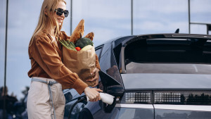Frau mit Einkaufstüte vor Elektroauto